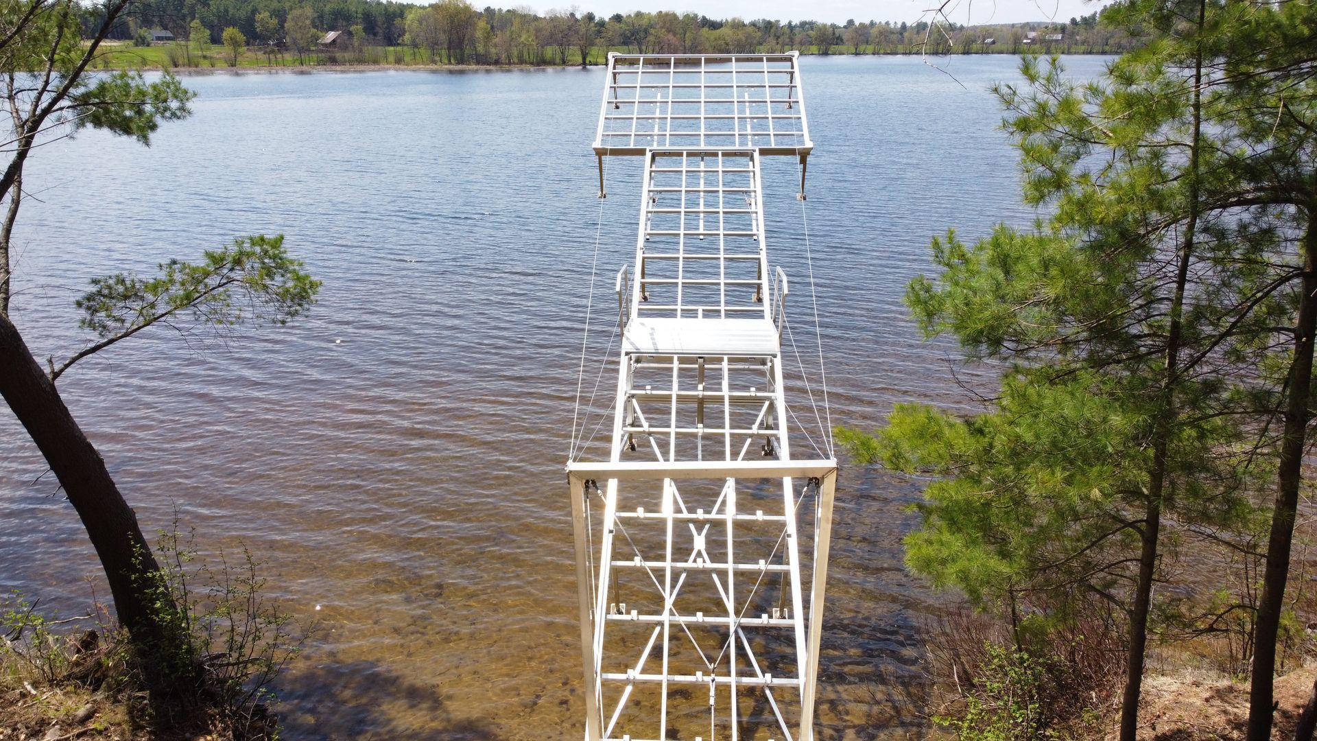 A white dock is sitting in the middle of a lake surrounded by trees.