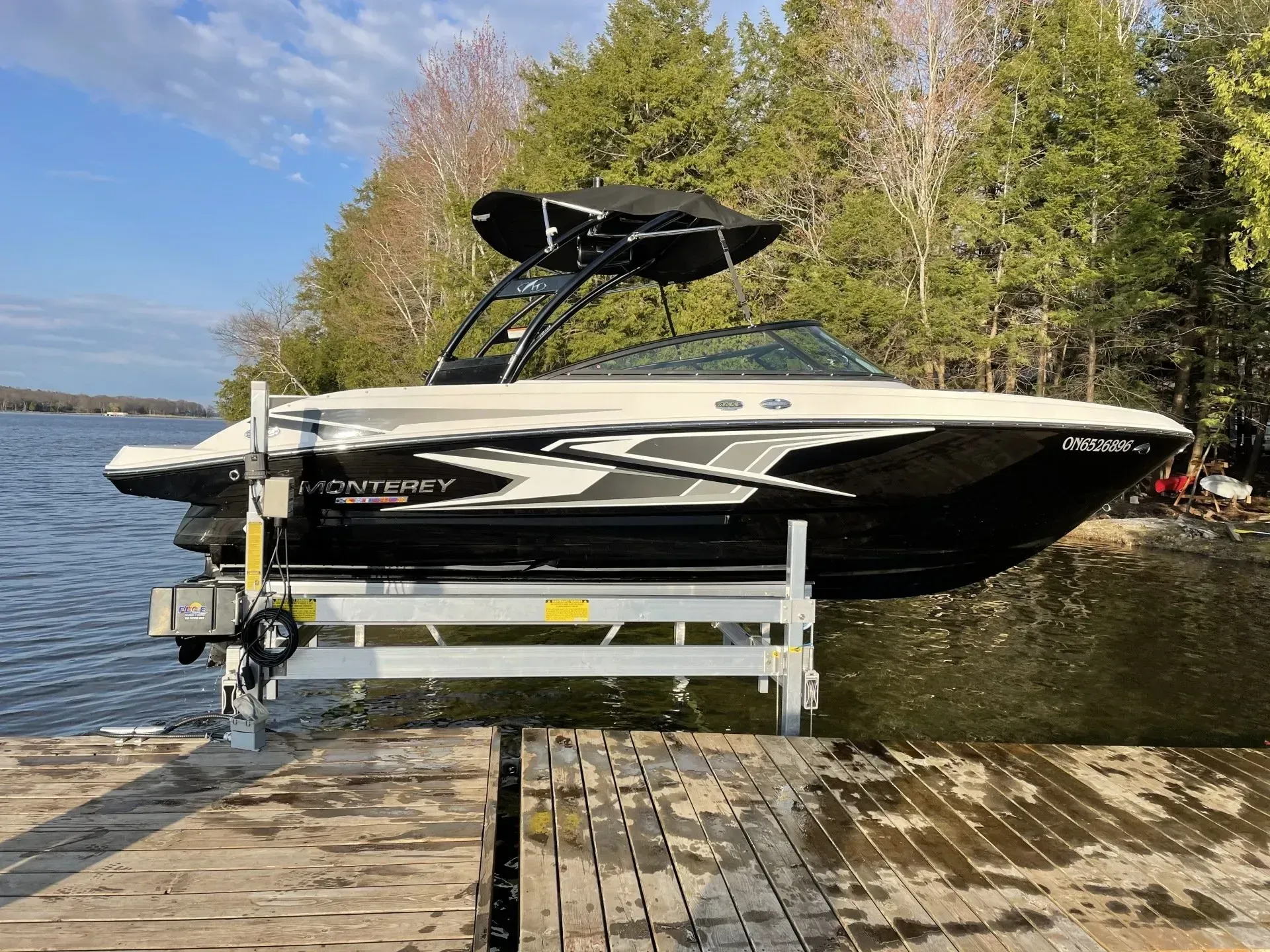 Boat lift supporting a recreational boat beside a dock on a calm lake.
