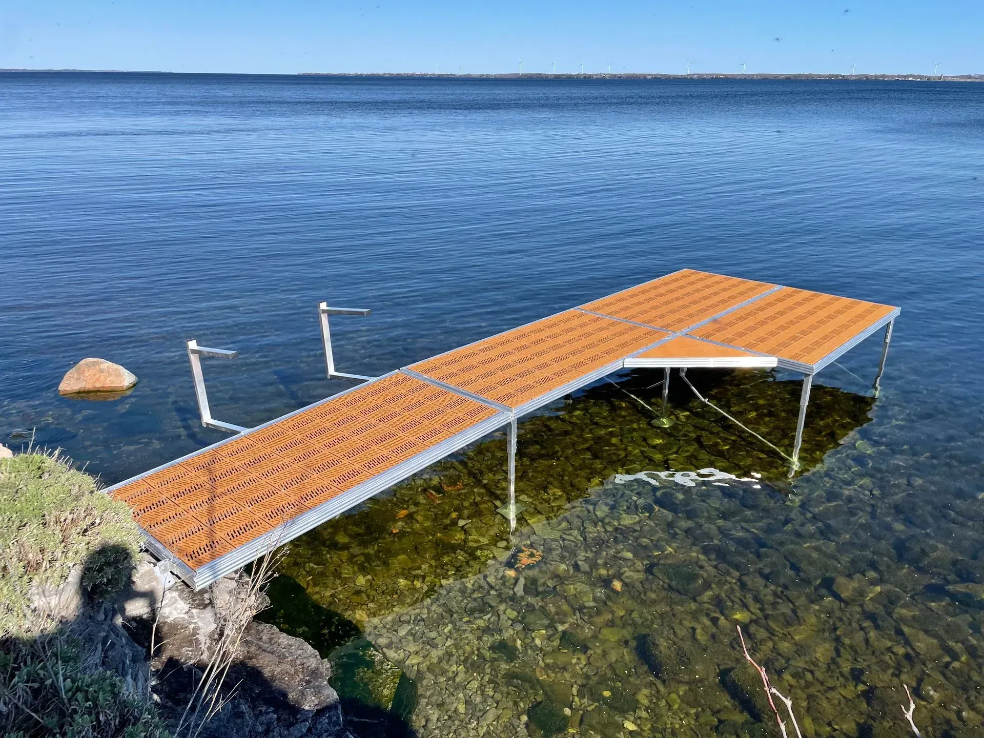 Aluminum frame dock with extending into clear shallow lake water with visible rocky lakebed.