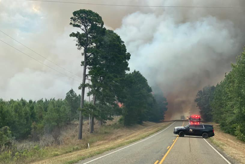 A police car is blocking a highway next to a forest fire.