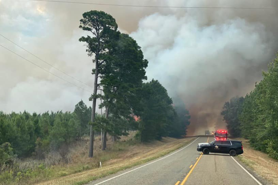 A police car is blocking a highway next to a forest fire.