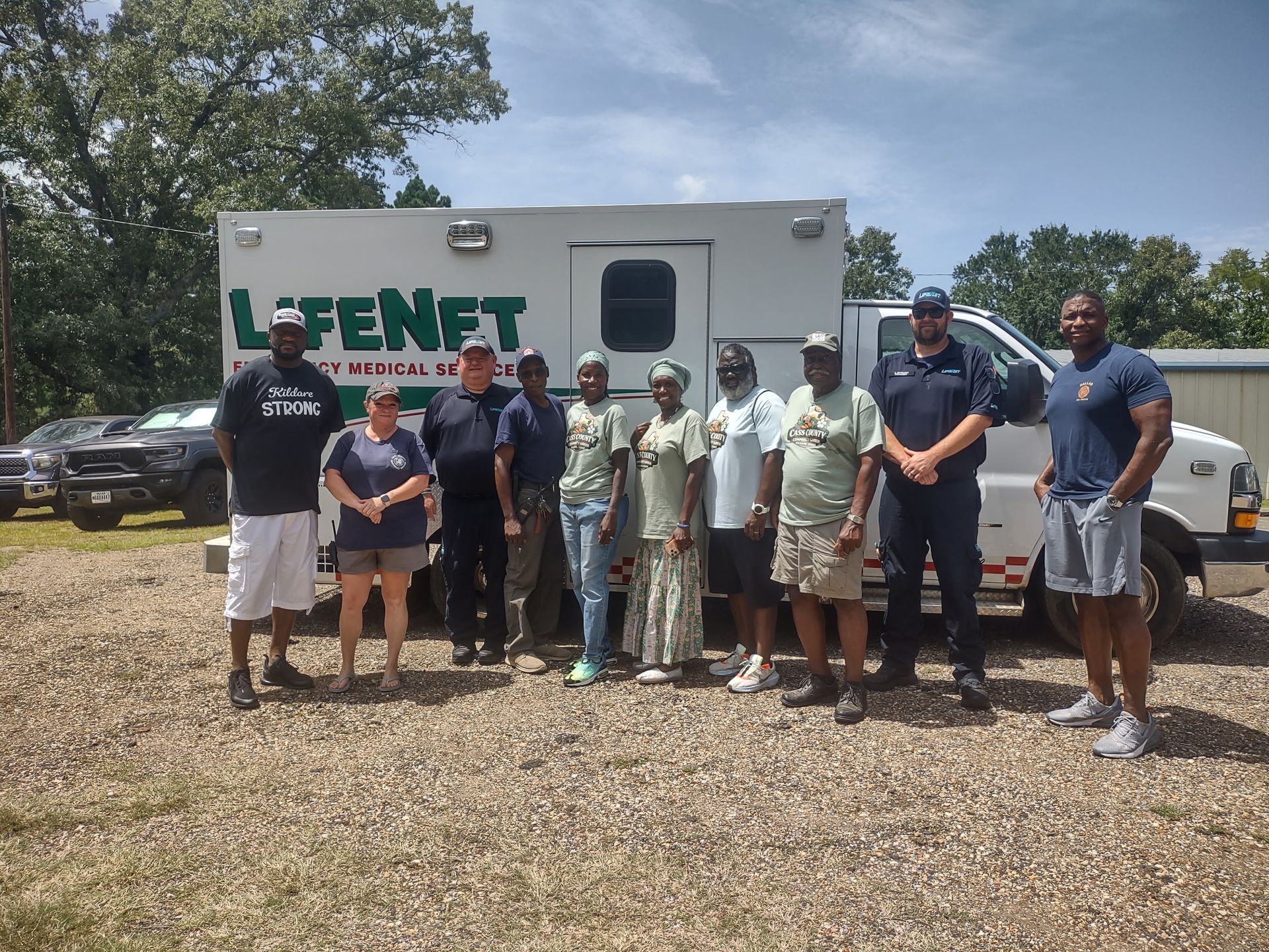 Group of people posing in front of a Fent trailer on a gravel lot, with trees and cars in the background.