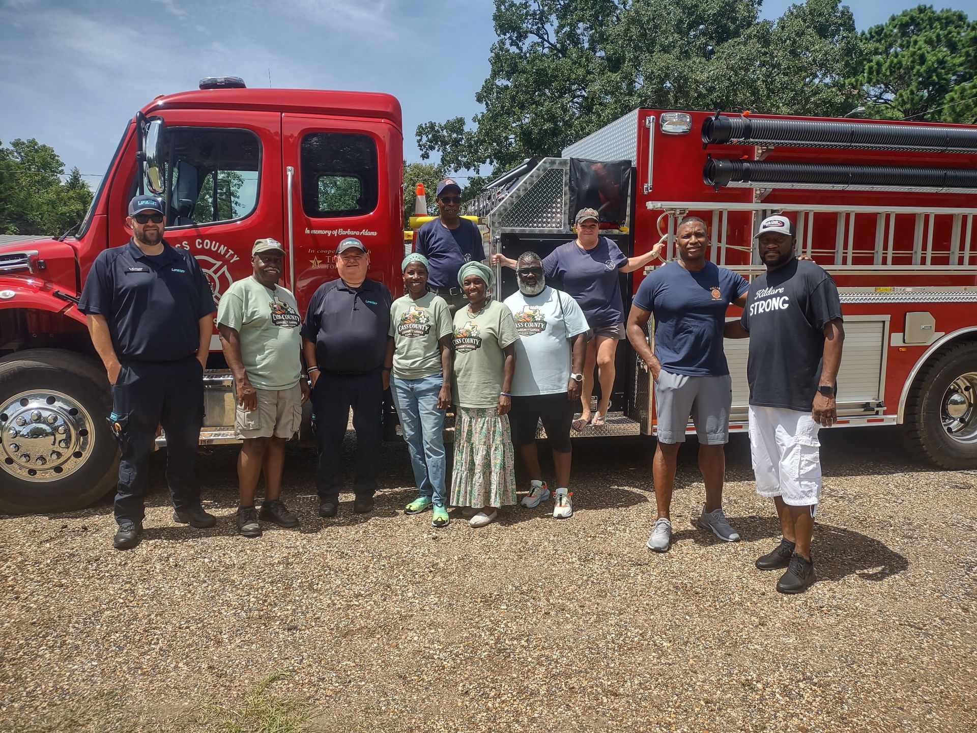 Group of people posing beside a red fire truck on a gravel lot outdoors