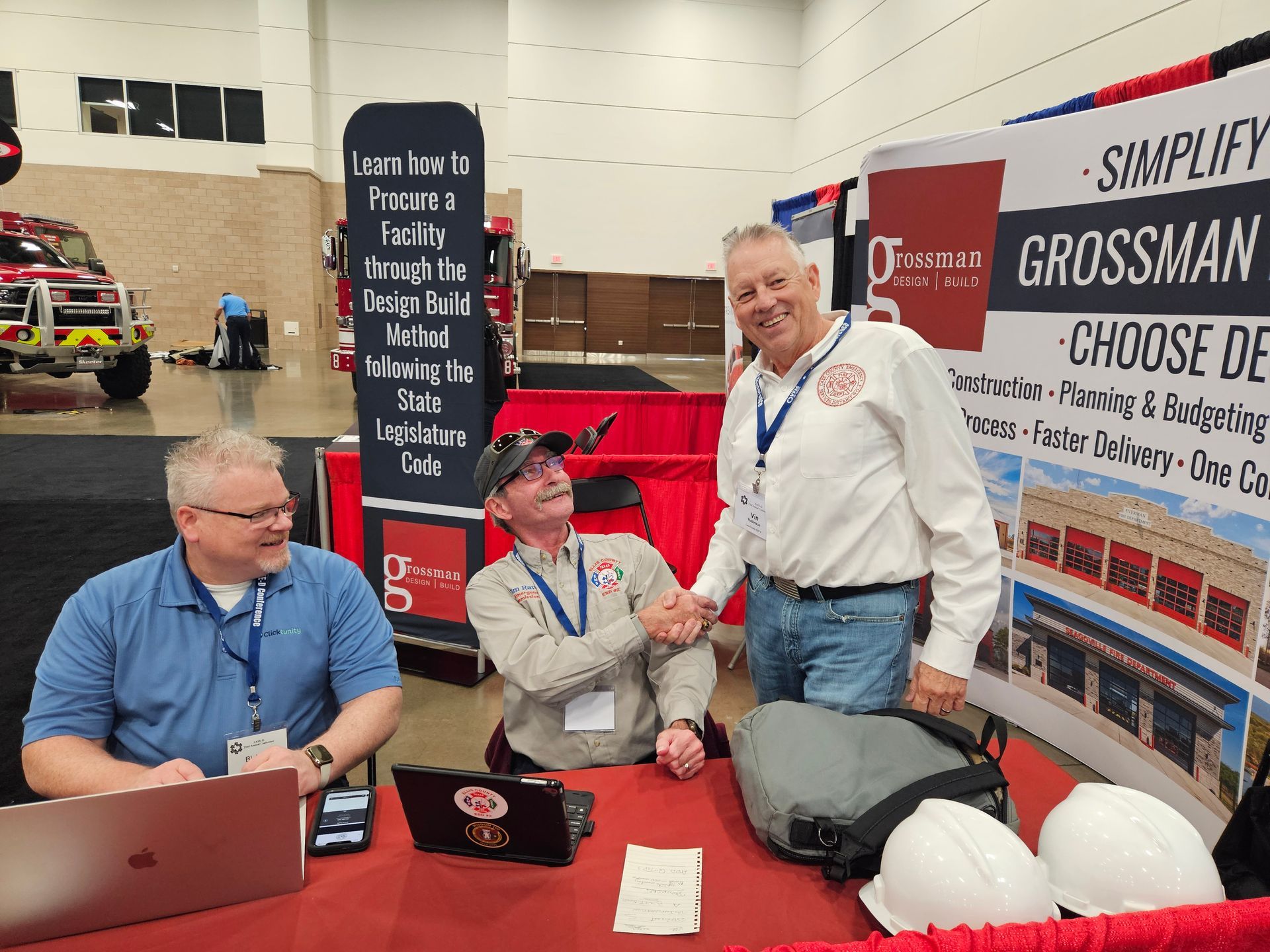 Three men are shaking hands at a booth at a convention.