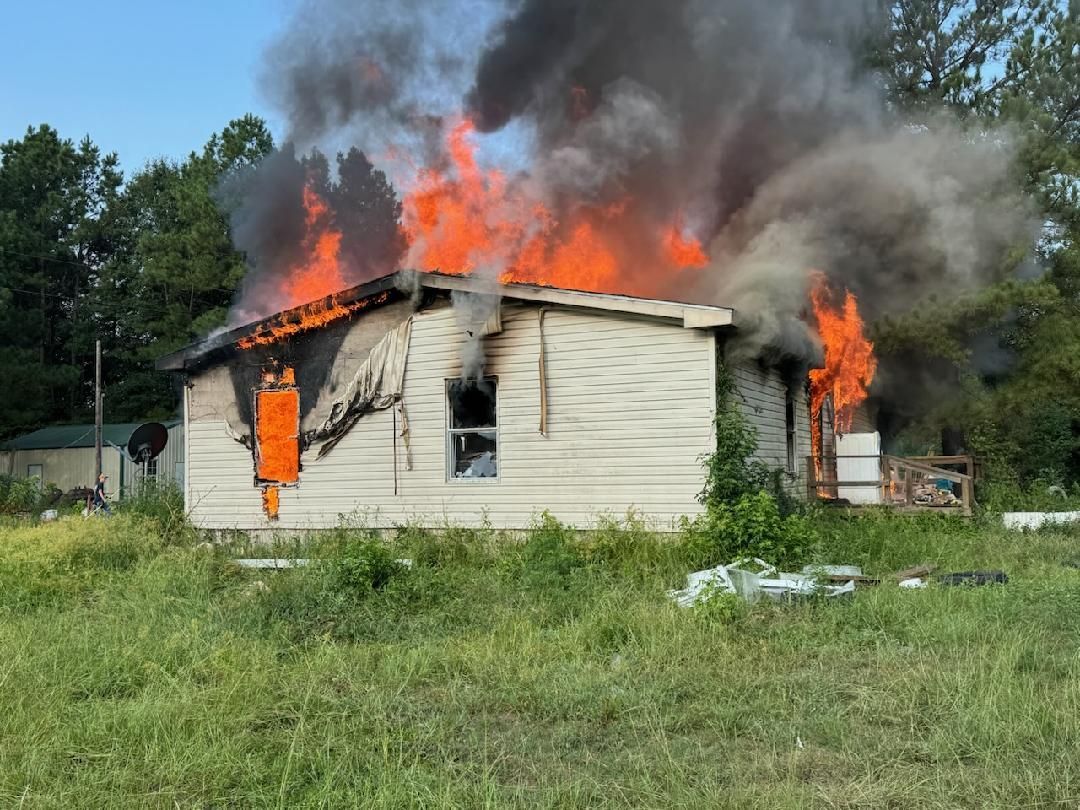 House engulfed in flames, thick black smoke billowing into the sky. Bright orange fire visible.