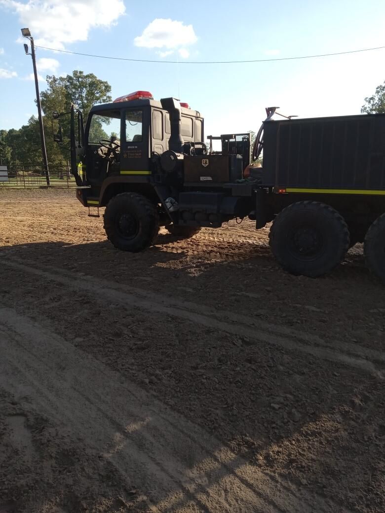 Dark-colored, heavy-duty truck with multiple wheels, likely for off-road use, parked on dirt.