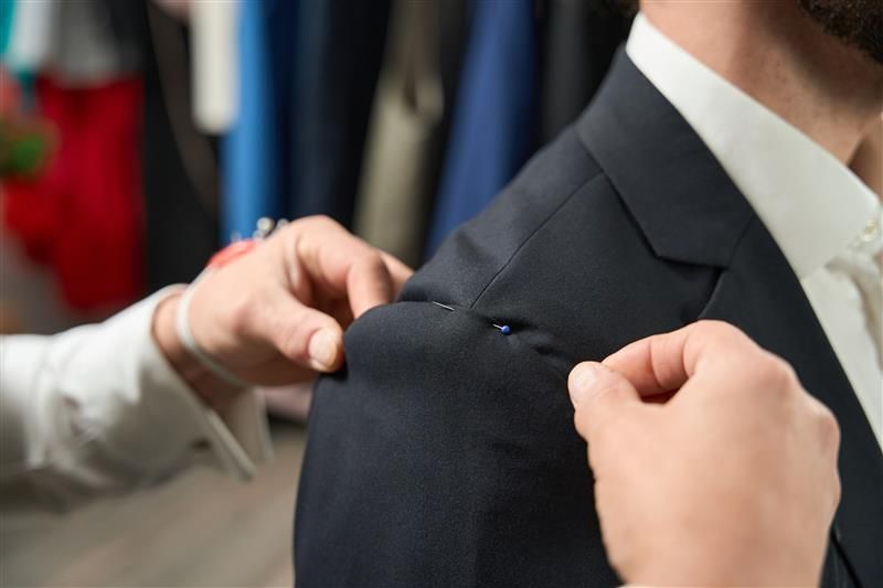 A close-up of a professional tailor adjusting a customer’s suit during a fitting session.