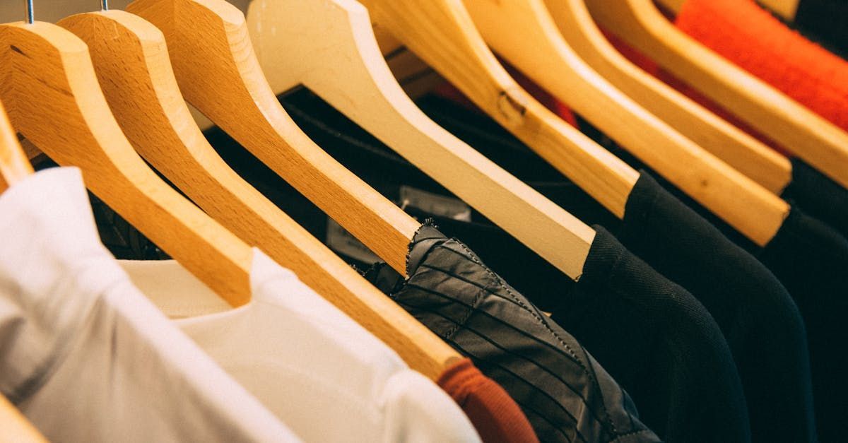 A row of clothes hanging on wooden hangers in a closet.