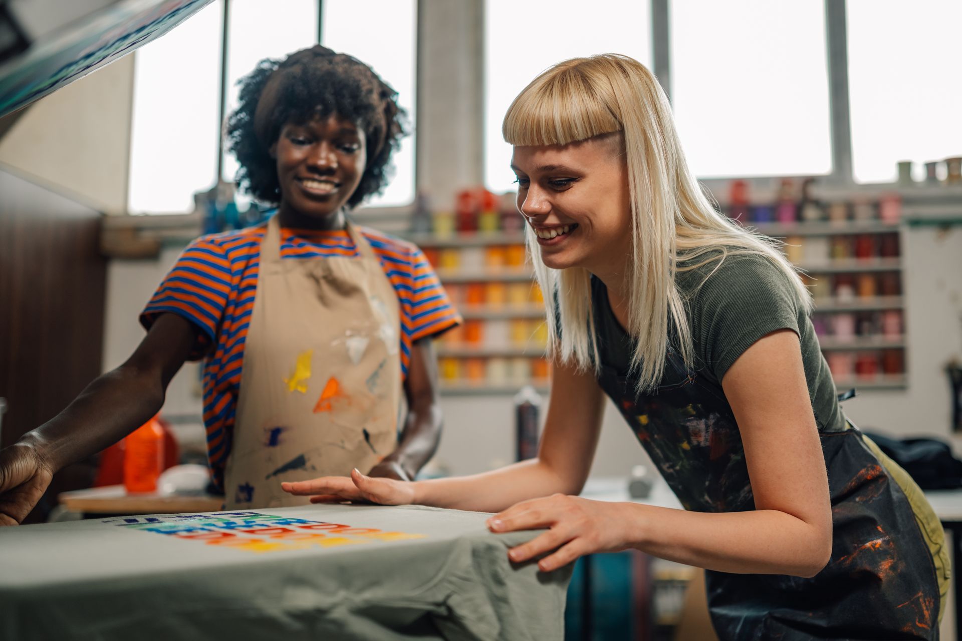 Two women are standing next to each other at a table in a workshop.