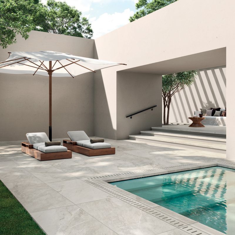 Een terras met stoelen en een parasol naast een zwembad