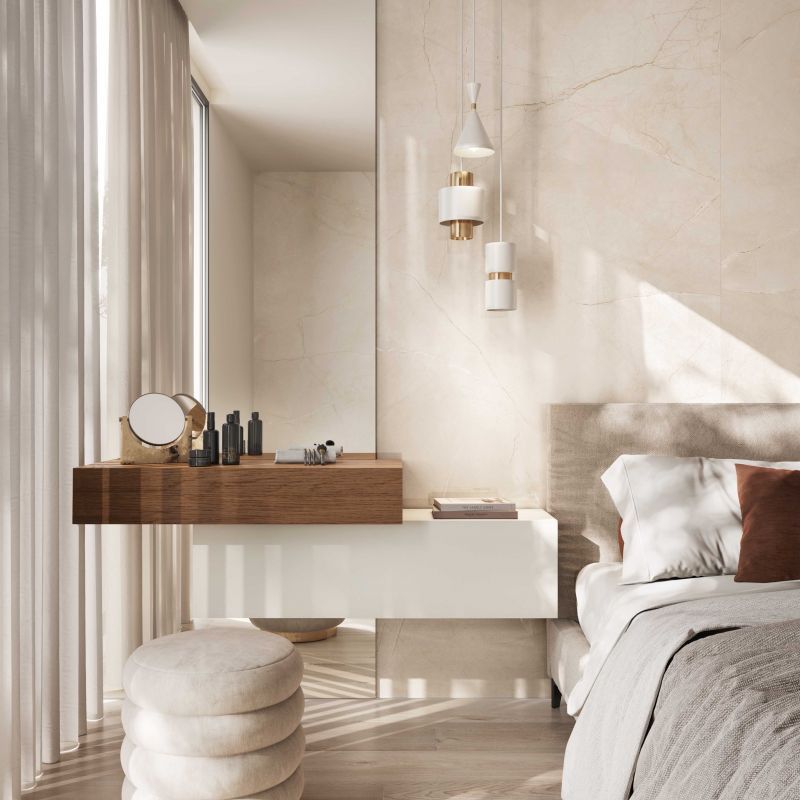 Een slaapkamer met een bed, ladekast, spiegel en voetenbankje.