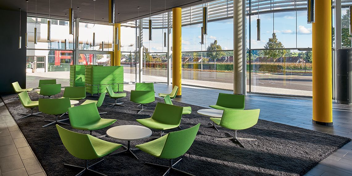 Een lobby met groene stoelen en tafels in een gebouw.