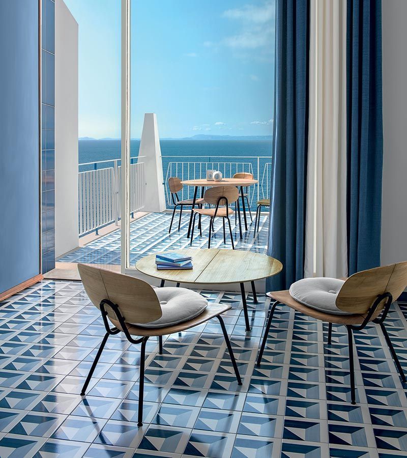 Een woonkamer met een tafel en stoelen en een balkon met uitzicht op de oceaan.