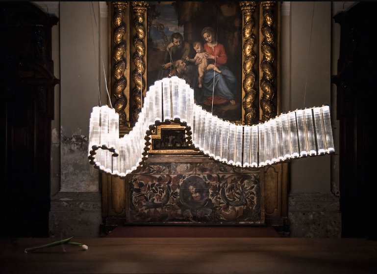 Een kroonluchter hangt voor een schilderij in een kerk.