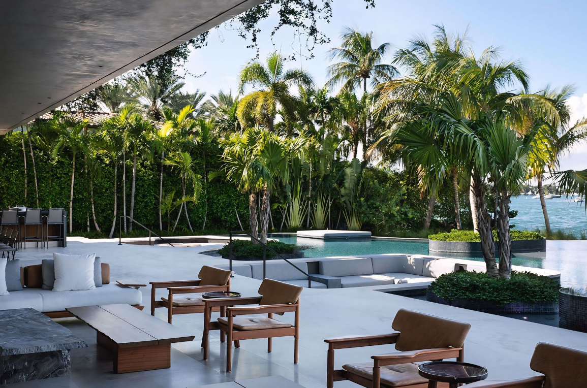 Een terras met stoelen en tafels voor een zwembad omgeven door palmbomen.