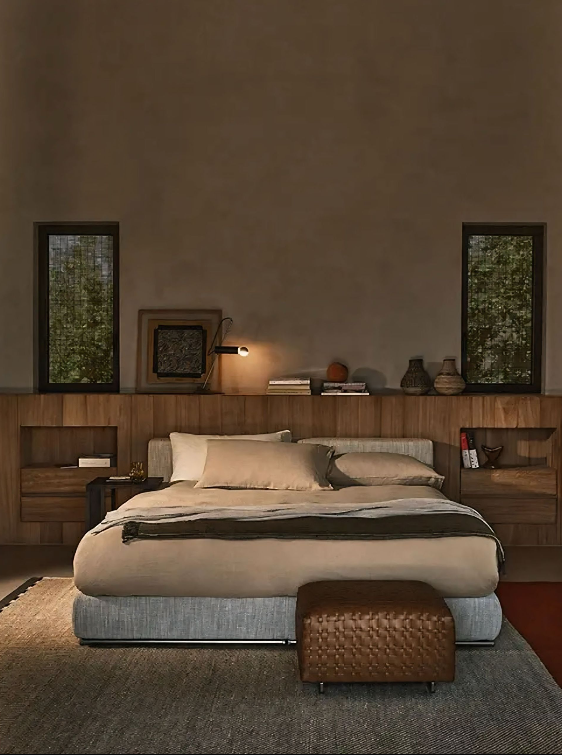 Een slaapkamer met een bed, een voetenbankje en twee ramen.