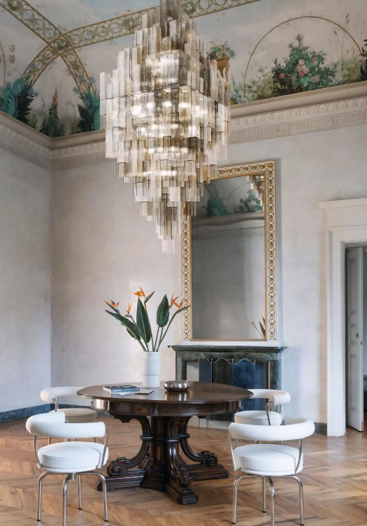 Een eetkamer met een tafel en stoelen en een grote kroonluchter die aan het plafond hangt.
