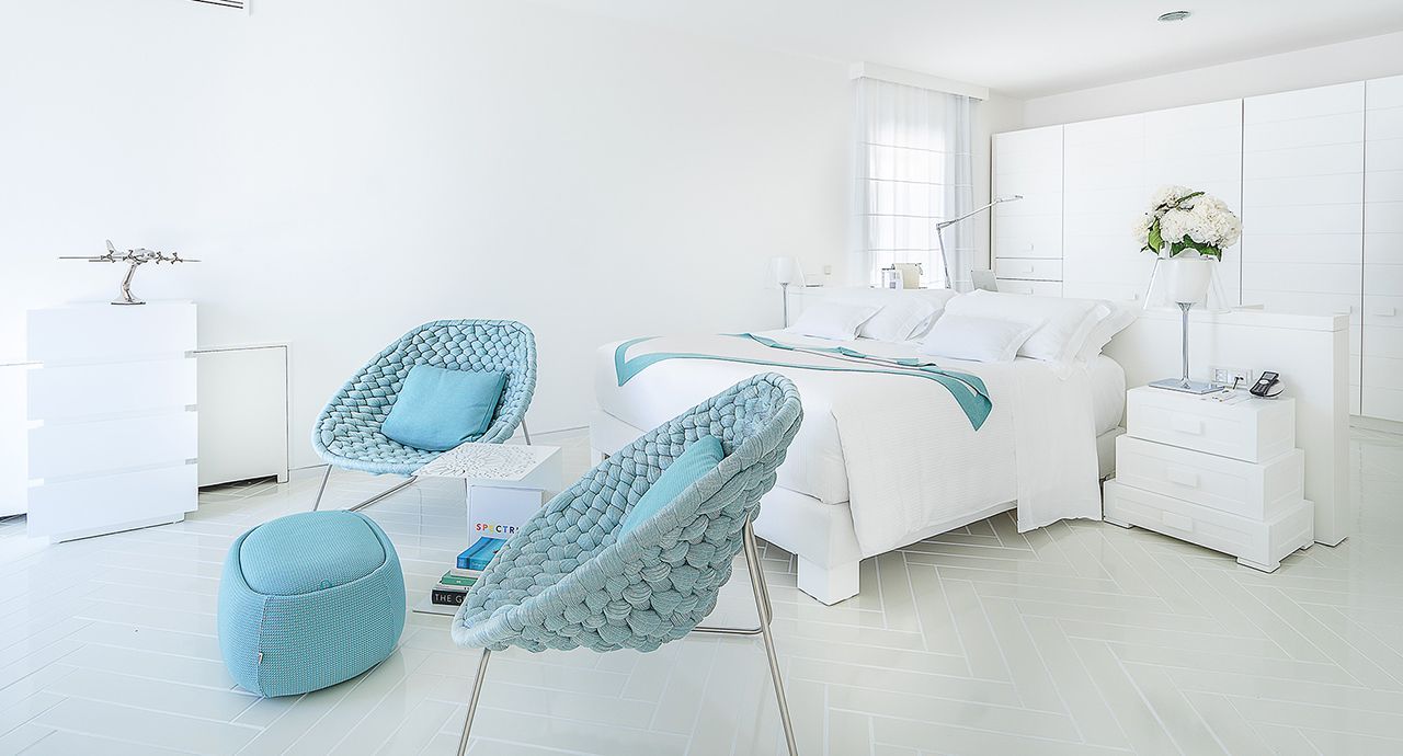 Een witte slaapkamer met blauwe stoelen en voetenbankjes