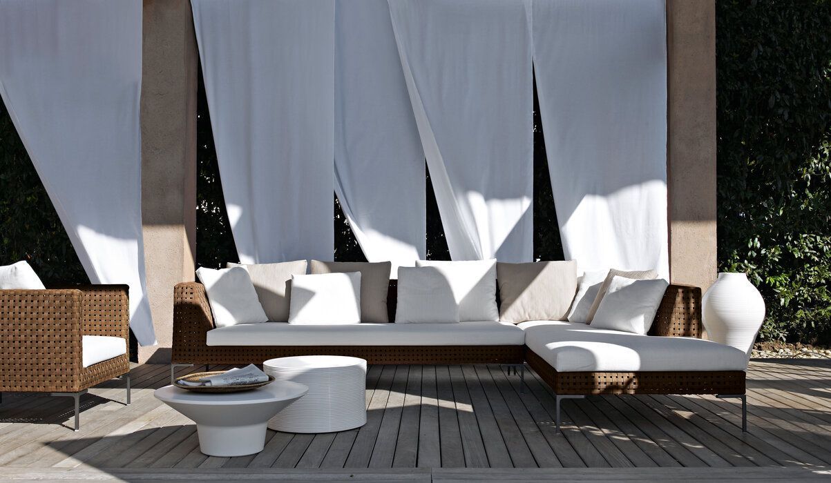 Een terras met een bank en stoelen onder witte gordijnen