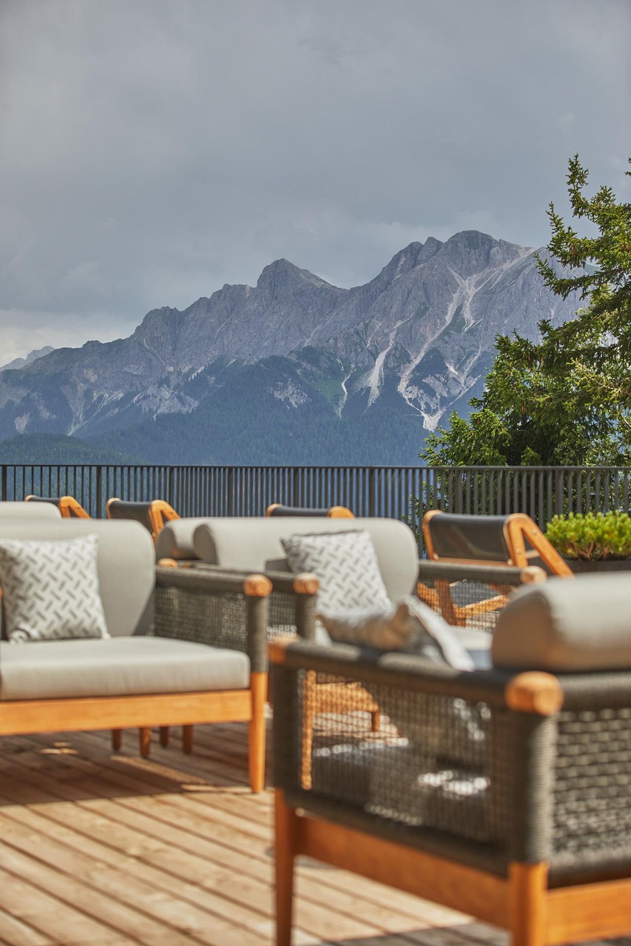 Een rij stoelen en een bank op een terras met bergen op de achtergrond.