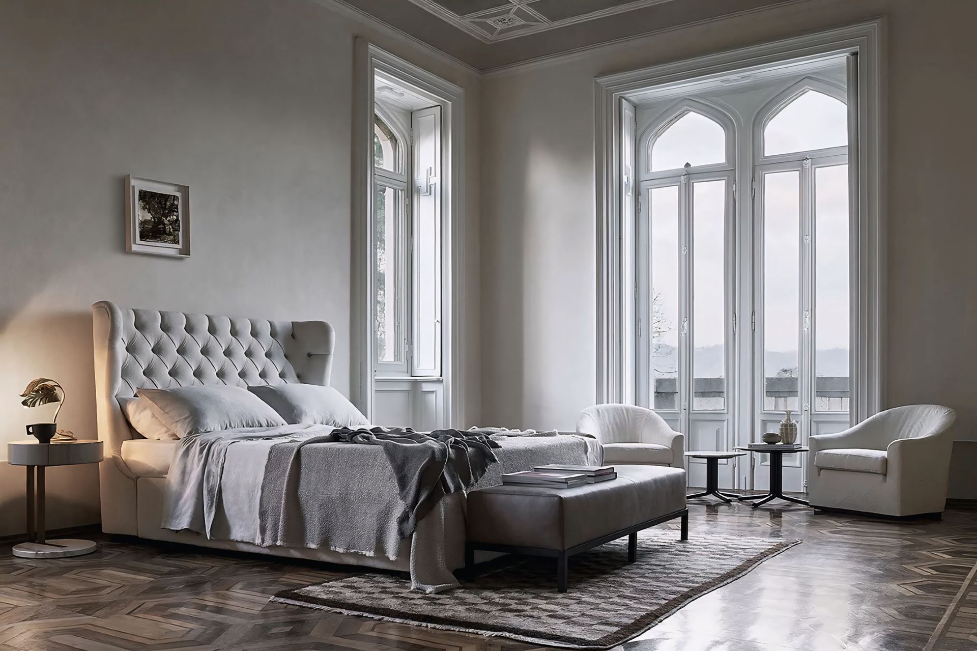 Een slaapkamer met een bed, stoelen, een voetenbankje en een groot raam.