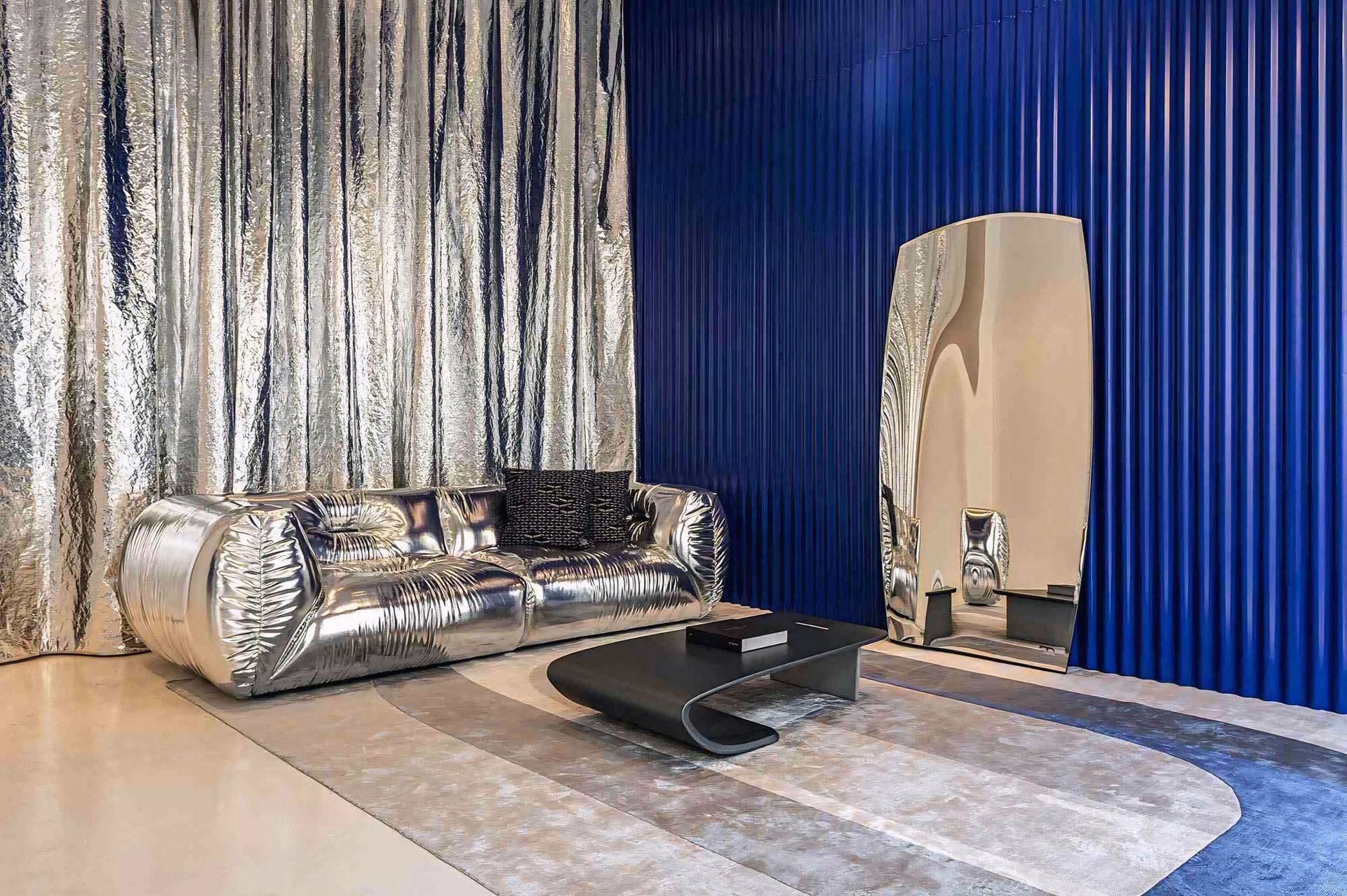 Een woonkamer met een zilveren bank en een blauwe muur.