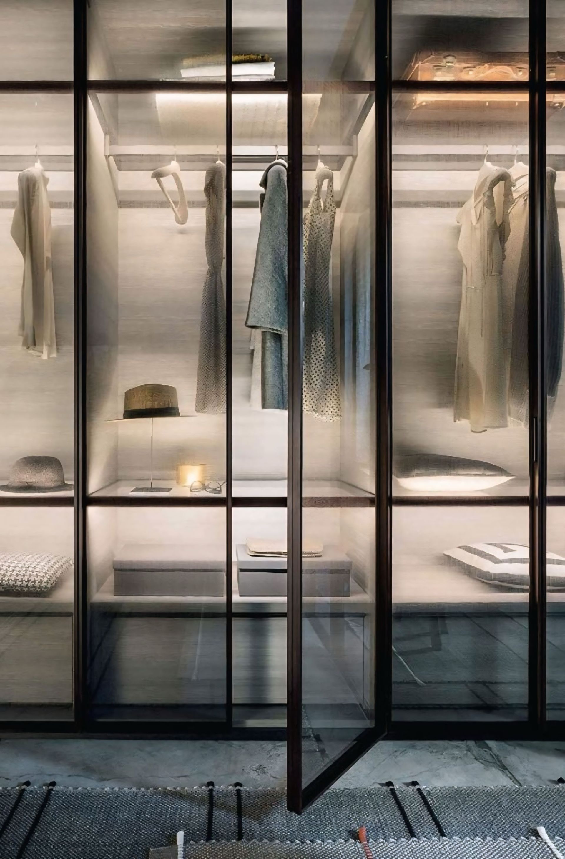 Een inloopkast met glazen deuren en planken vol kleding.