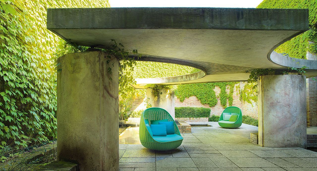 Een terras met groene stoelen onder een betonnen luifel.