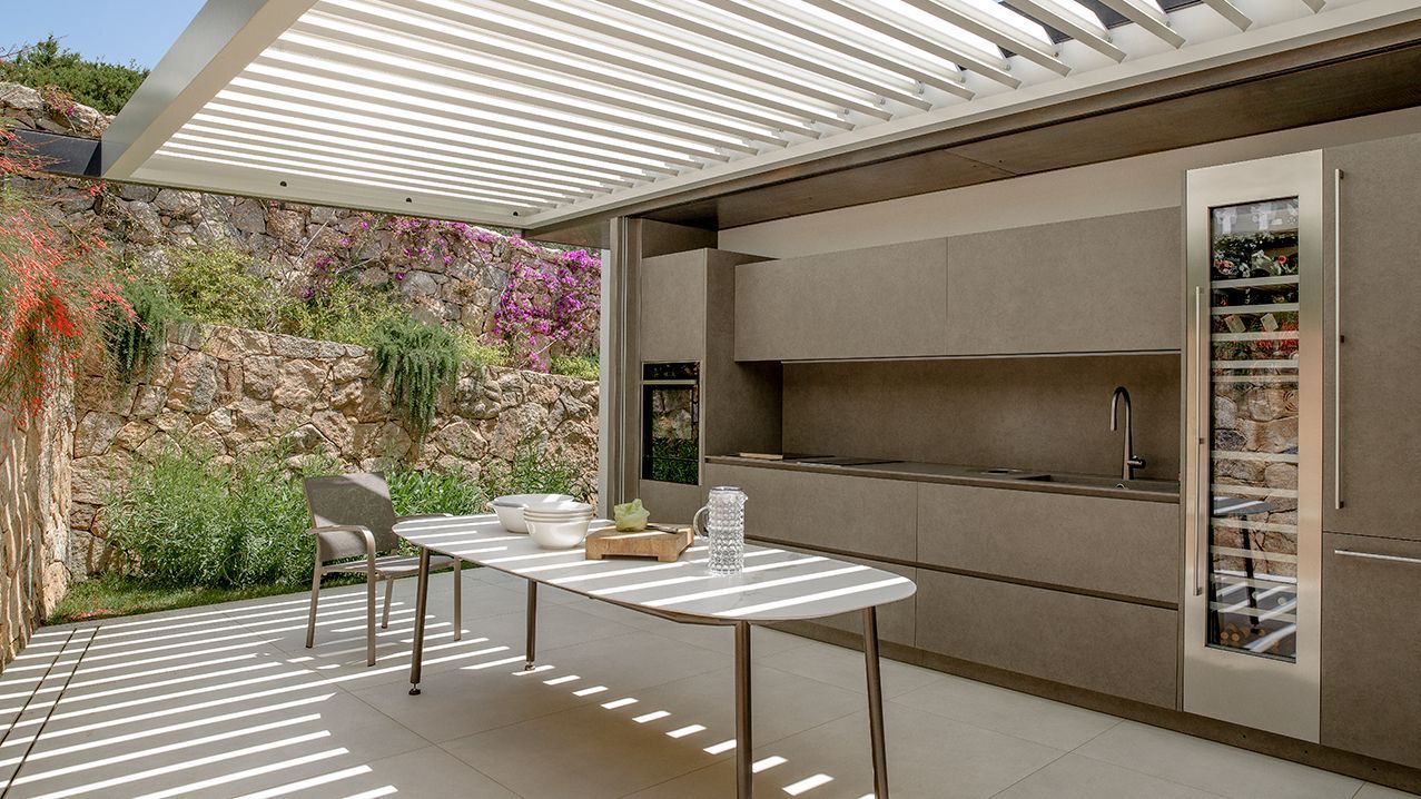 Een keuken met een tafel en stoelen onder een pergola.