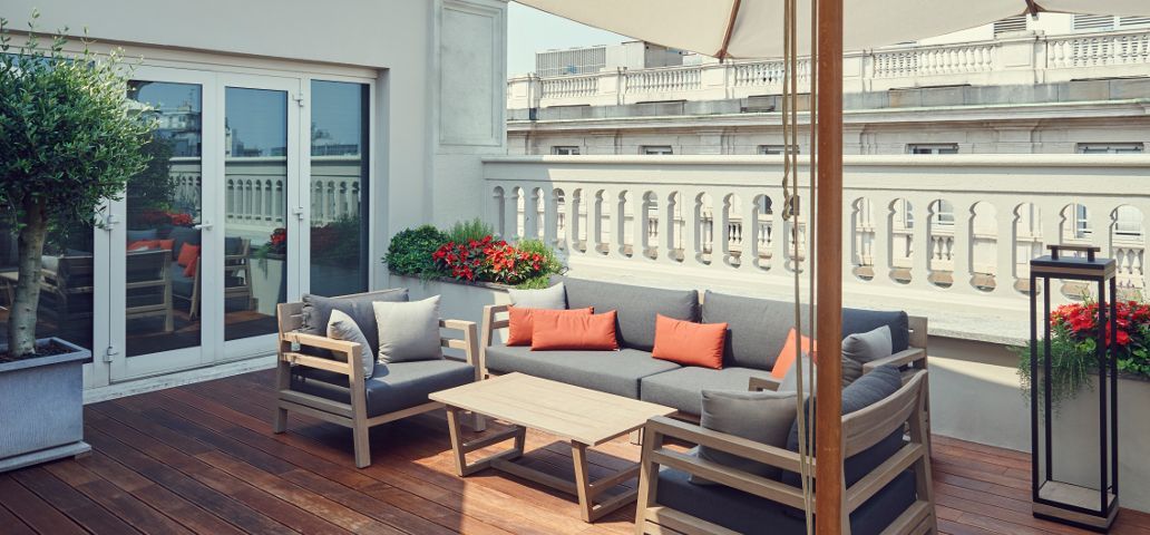 Een balkon met een bank, stoelen, tafel en parasol.