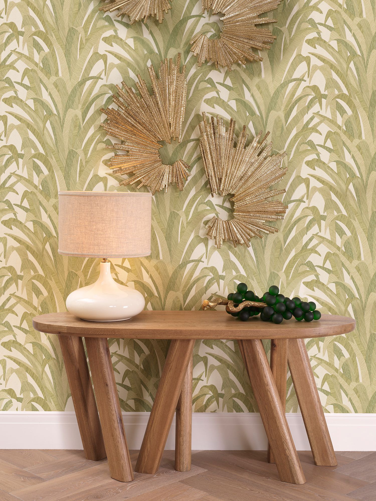 Een tafel met een lamp erop voor een muur met bladeren erop.