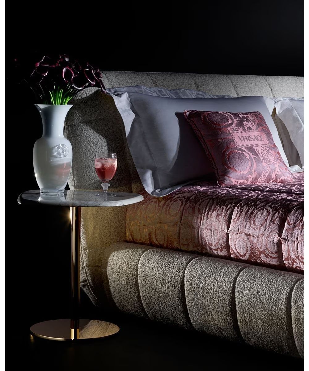 Een bed met een vaas met bloemen en een glas wijn op een tafel