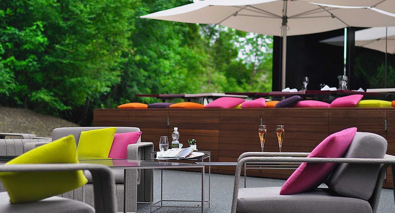 Een terras met stoelen, tafels, parasols en kussens.
