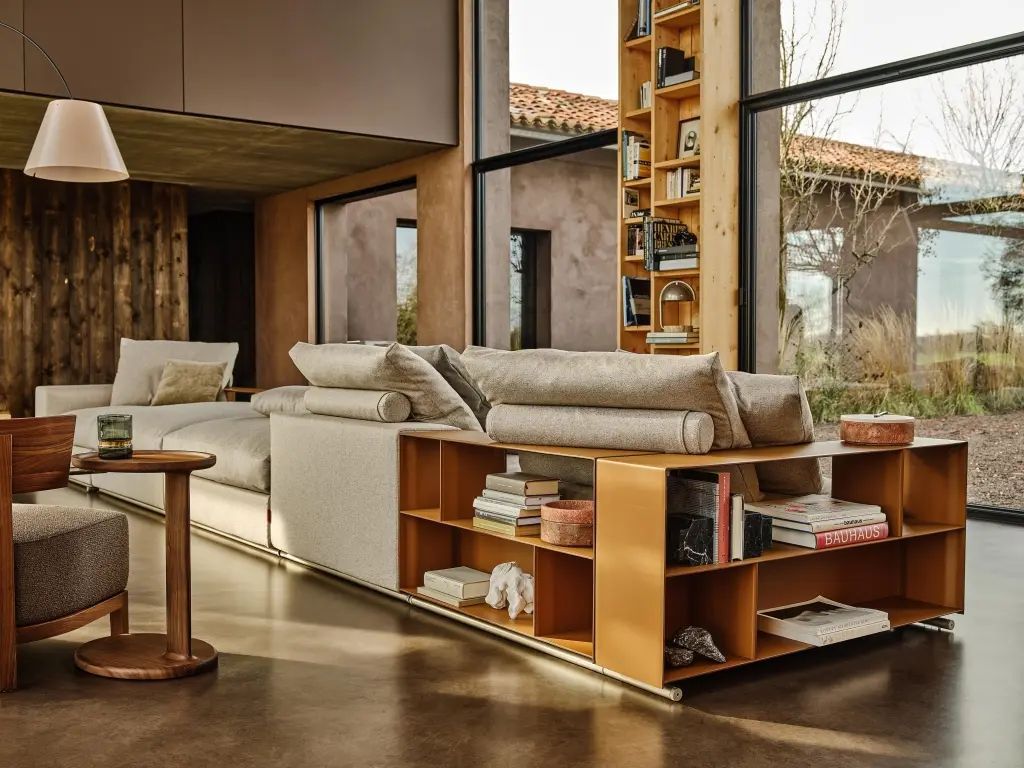 Een woonkamer met een bank, stoelen, boekenplanken en een groot raam.