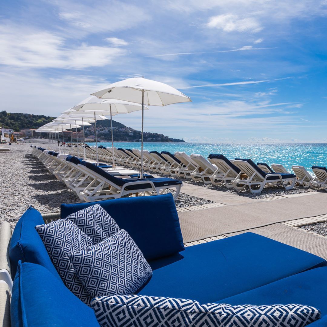 Een blauwe bank staat op het strand naast een rij stoelen en parasols.