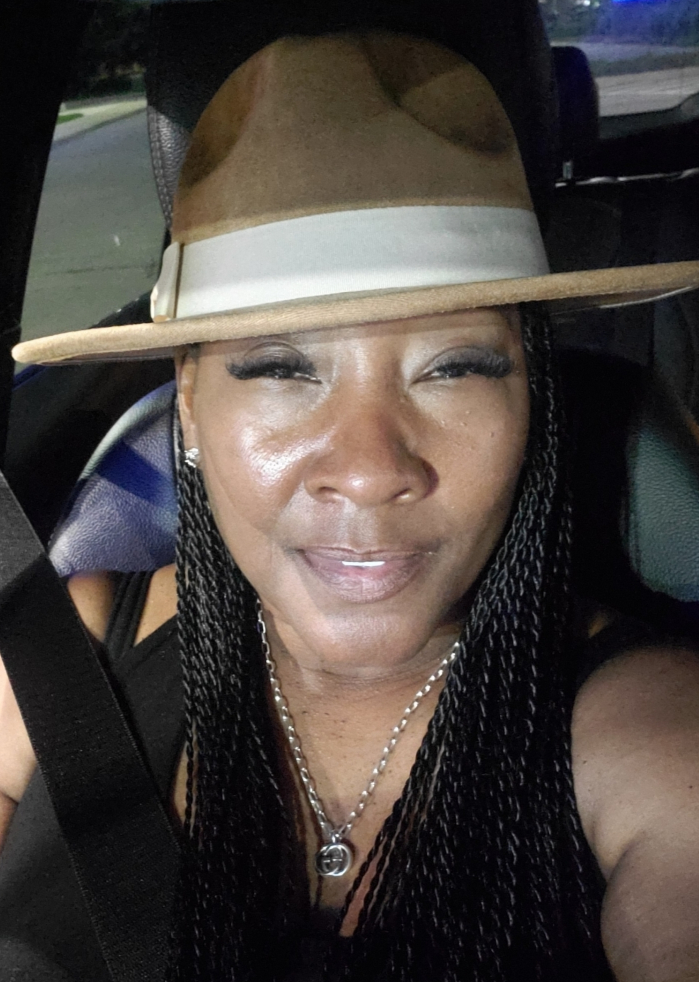 A woman wearing a hat and a necklace is sitting in a car.