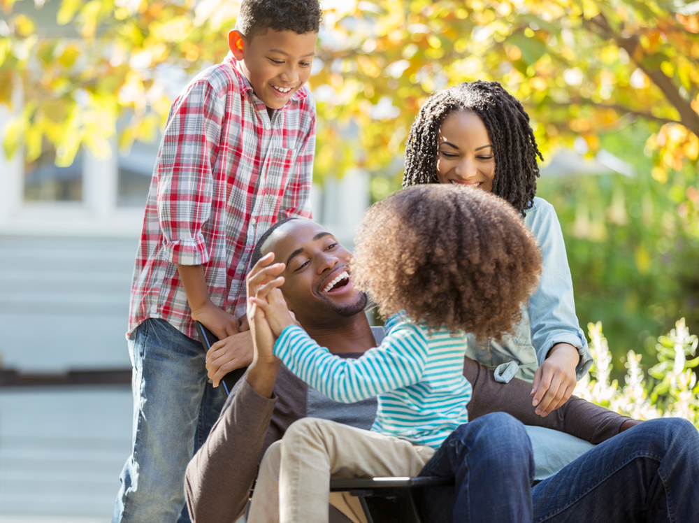 A man in a wheelchair is sitting next to a woman and two children.
