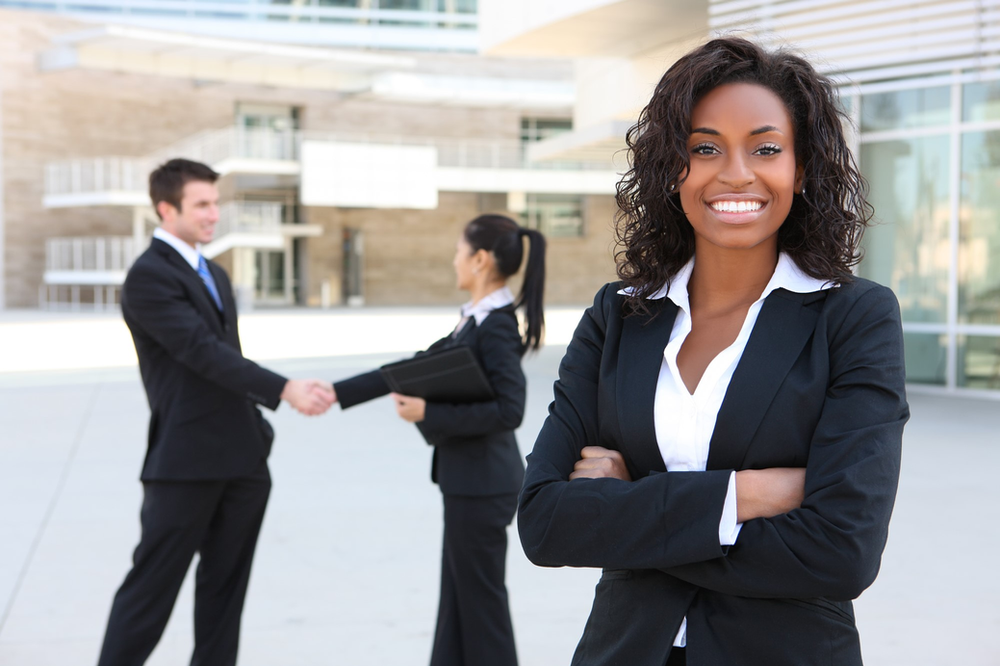 A woman with her arms crossed is standing in front of a group of business people shaking hands A woman with her arms crossed stands in front of a group of business people shaking hands