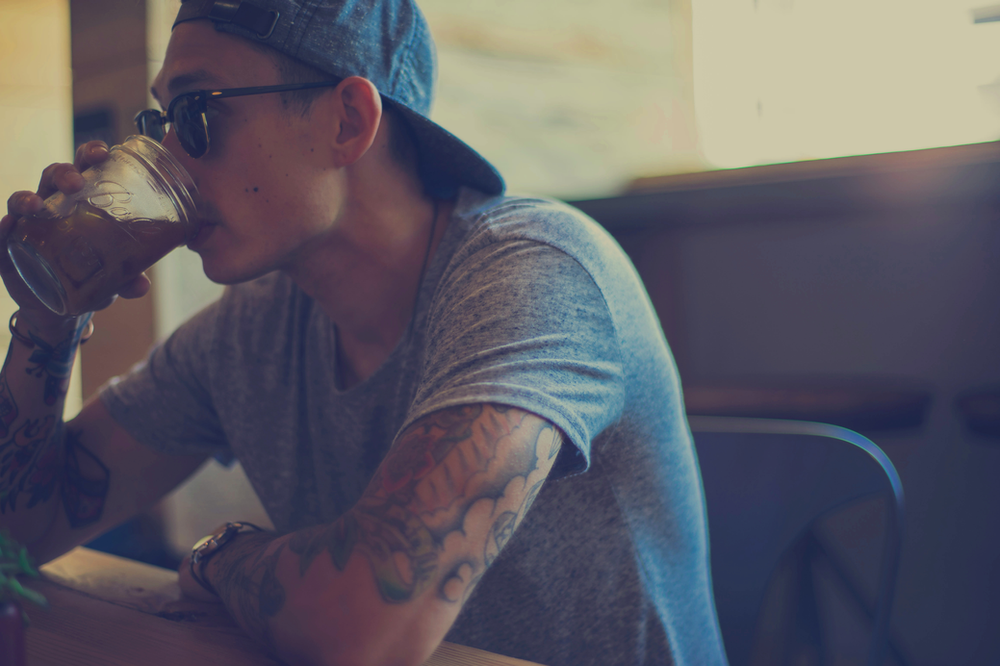 A man with tattoos is drinking from a cup while sitting at a table.