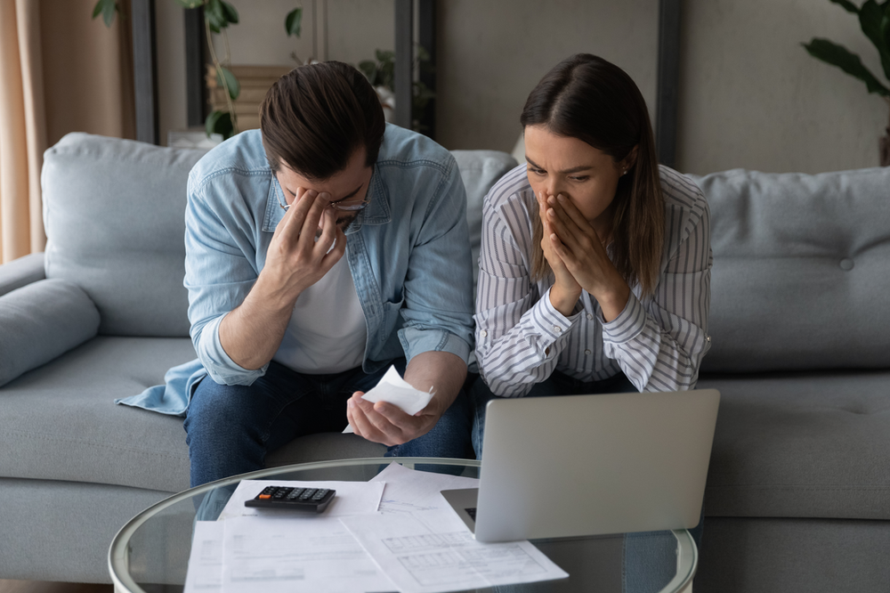 A man and a woman are sitting on a couch looking at their bills.