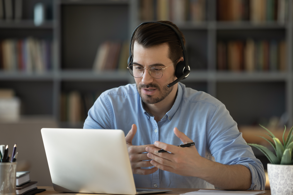 A man wearing headphones is sitting in front of a laptop computer. A man wearing headphones is sitting in front of a laptop computer.