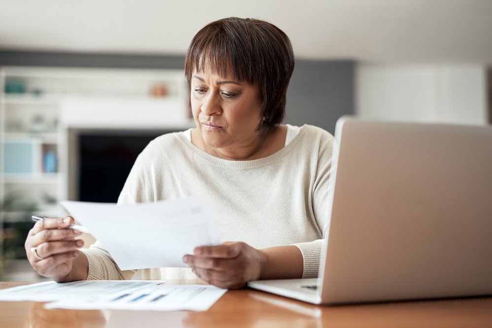 A woman is sitting at a table with a laptop and a piece of paper.