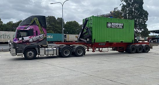 A semi truck is carrying a green container on a trailer — Newport Recycling in Woree, QLD