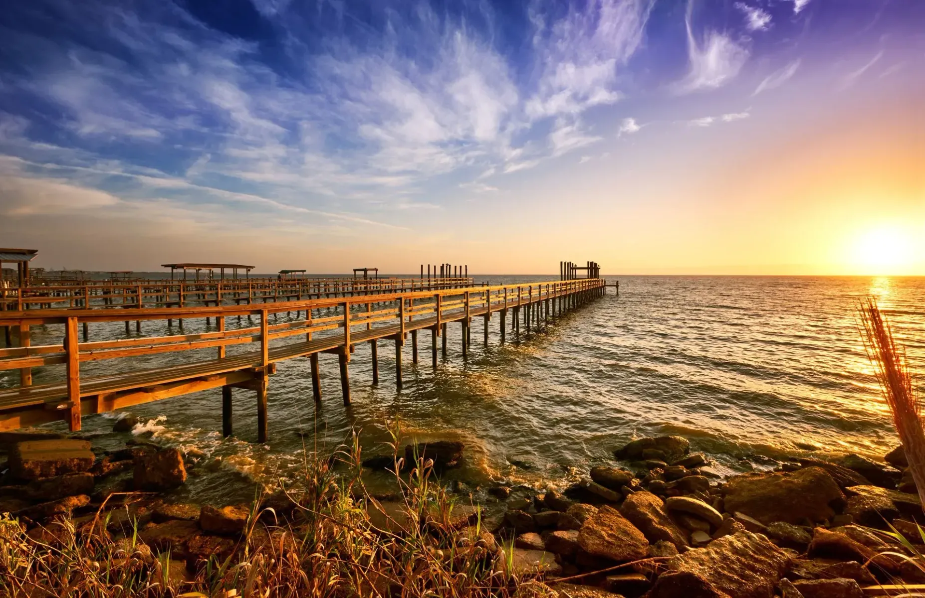 Sunset over a wooden pier extending into a rippling sea, with warm orange light and dramatic clouds