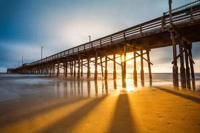 Sunset over a wooden pier stretching across a sandy beach, with long shadows and glowing reflections