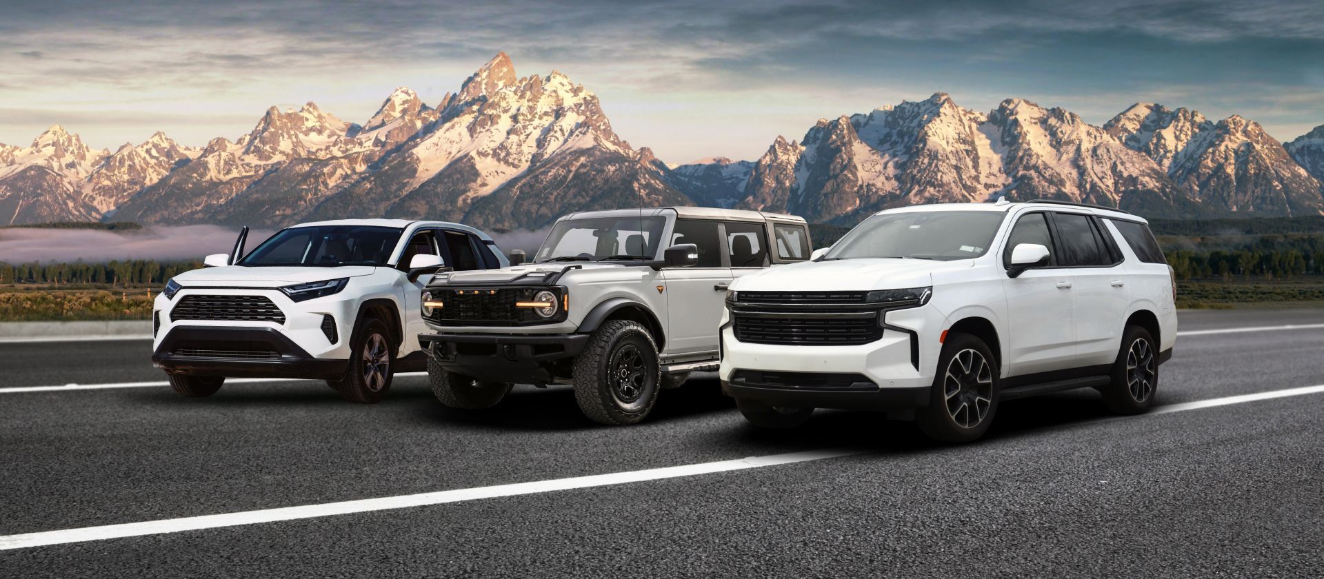 Three pickup trucks parked on a road with snowy mountains in the background. | Madison Automotive
