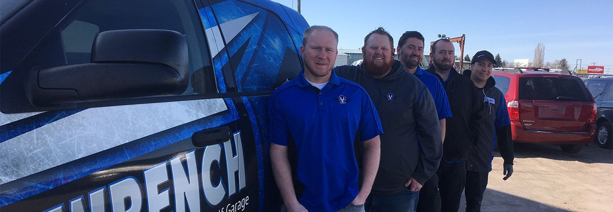 Group of people standing beside a blue branded vehicle outdoors on a sunny day. | Madison Automotive