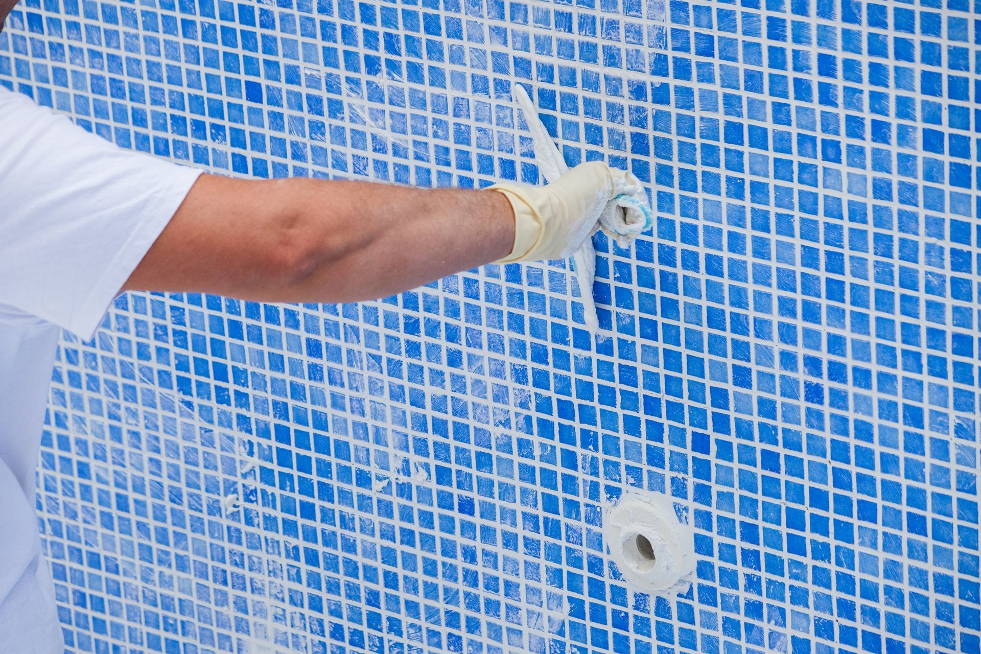 Pool renovation work. A worker lays the tiles and covers the seams in the pool.