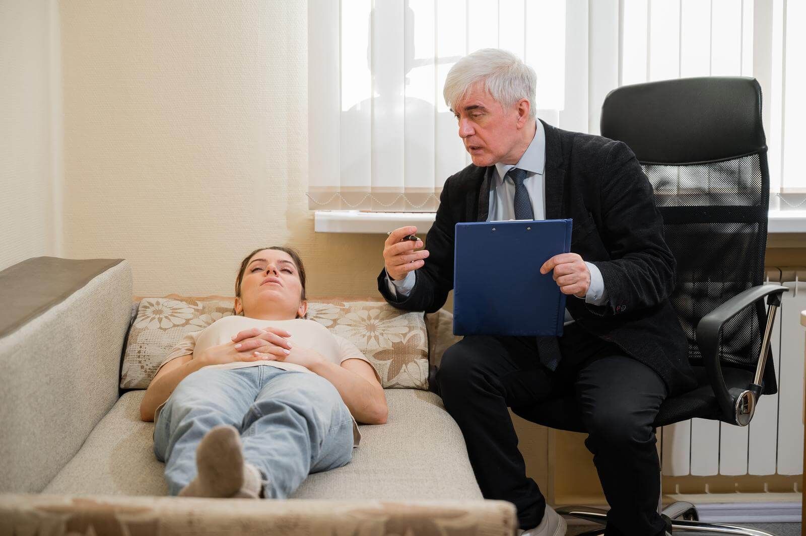 photo of a therapist in his chair hypnotizing his client who is laying down comfortably on a couch