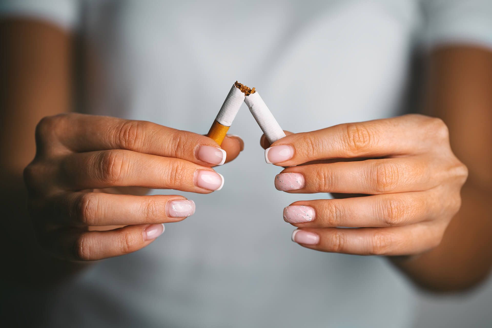A woman is breaking a cigarette into two pieces with her hands.